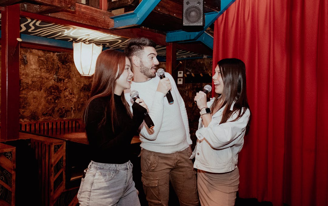 Three people doing Karaoke next to a red curtain. 