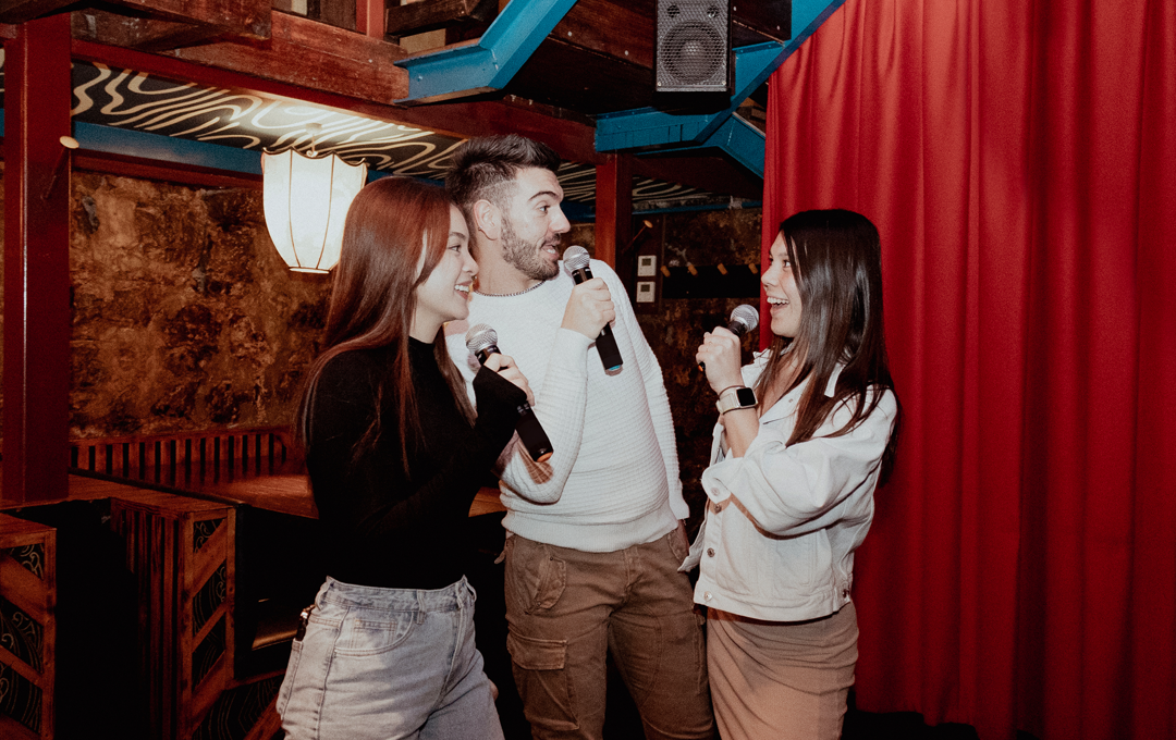 Three people doing Karaoke next to a red curtain. 