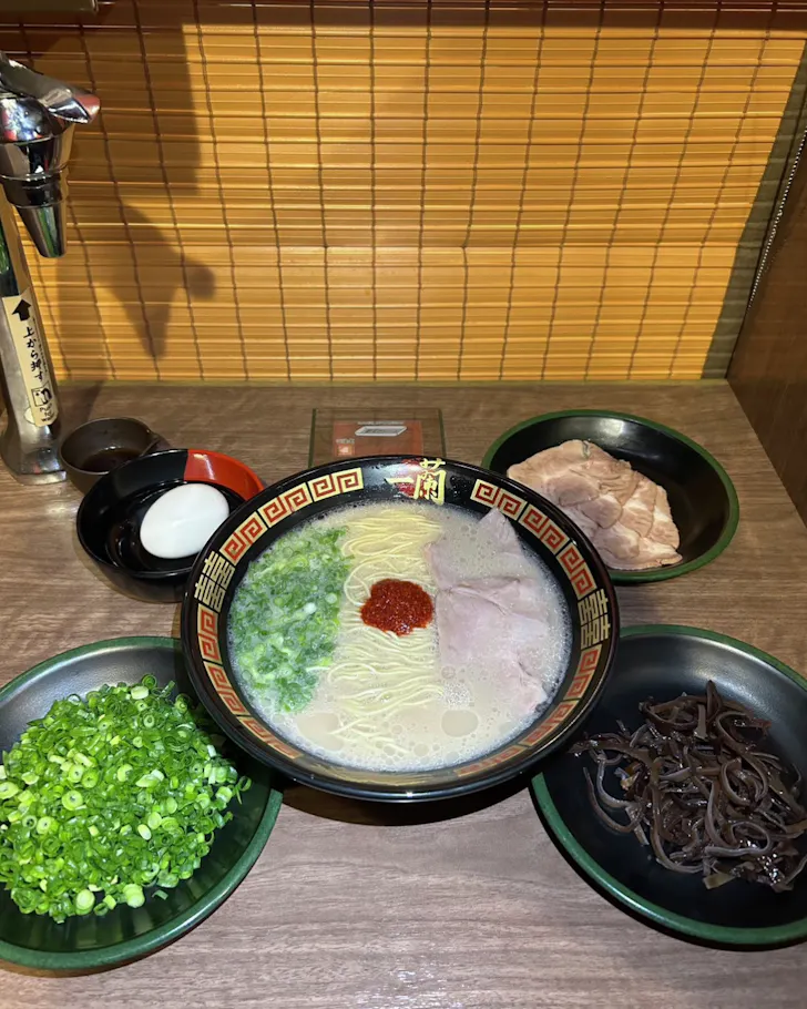 A bowl of ramen and add-ons like a boiled egg and green onions spread out on a table in Ichiran Ramen Osaka.