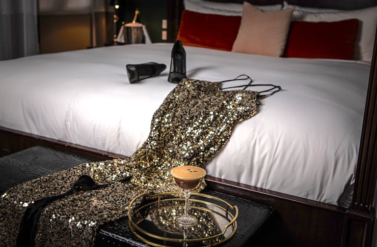 A sequinned dress rests on a hotel bed behind an espresso martini
