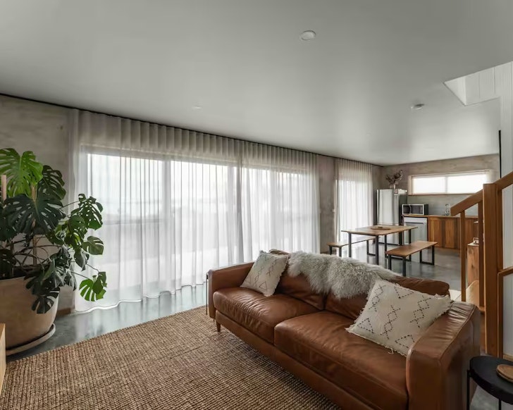 A cosy lounge with a brown couch and a sleek timber kitchen
