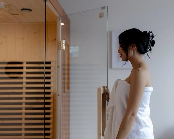 A woman in a towel opens the door to an infrared sauna. 