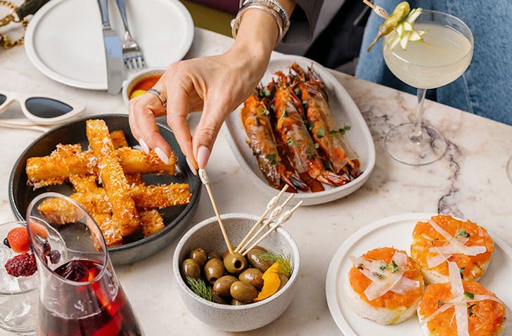 A table of various dishes with a hand reaching over using a toothpick to pick up olives