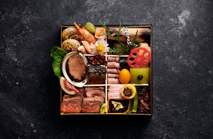 A tidy bento box full of different Japanese dishes on a black stone bench. 