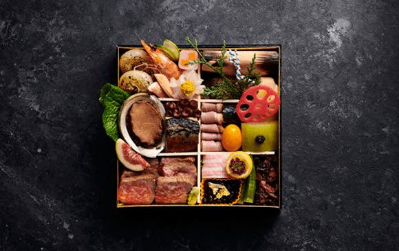 A tidy bento box full of different Japanese dishes on a black stone bench. 