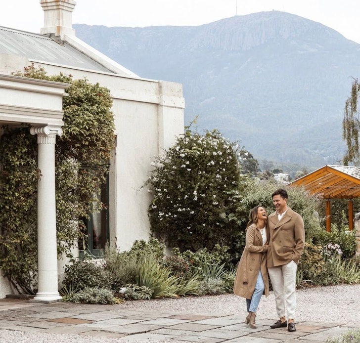 A couple walks arm in arm at the Islington Hotel one of the best hotels in Tasmania with mountains in the background