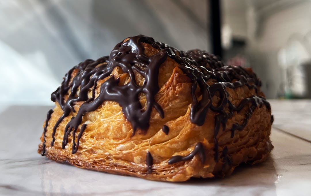 A croissant covered in drizzles of chocolate sauce. 