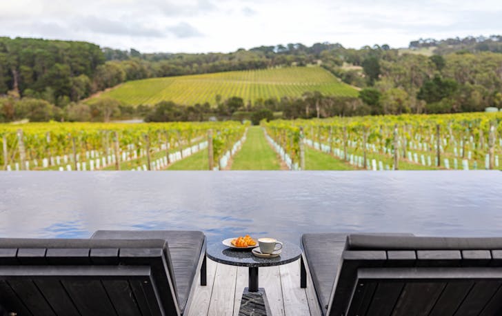 Two pool chairs overlooking a large vineyard at a best winery accommodation Victoria.