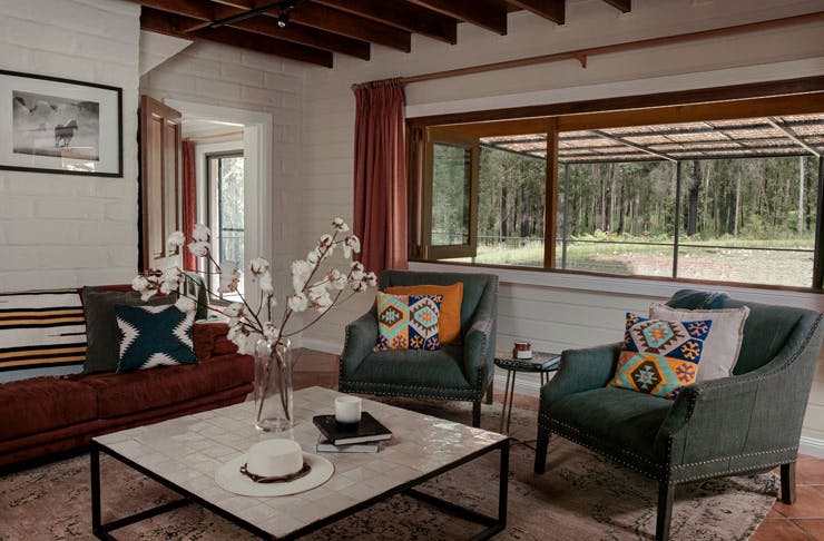 A living room with plush olive green couches and a wide open window looking out onto a lake. 