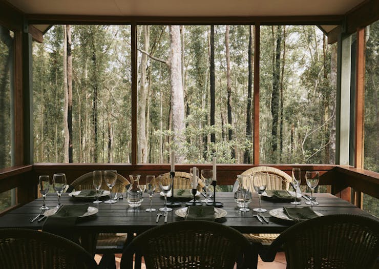 A dining table on a deck overlooking bushland. 