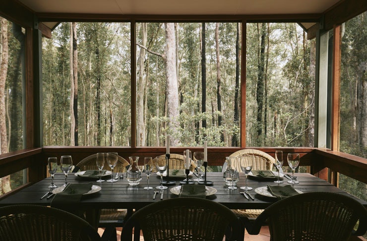 A dining table on a deck overlooking bushland. 