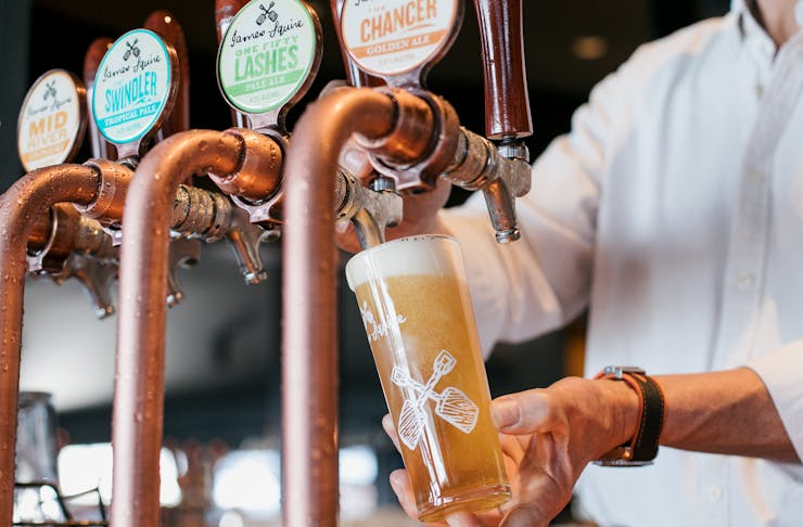A barman pours a beer into a glass from a copper tap at a James Squire brewhouse.