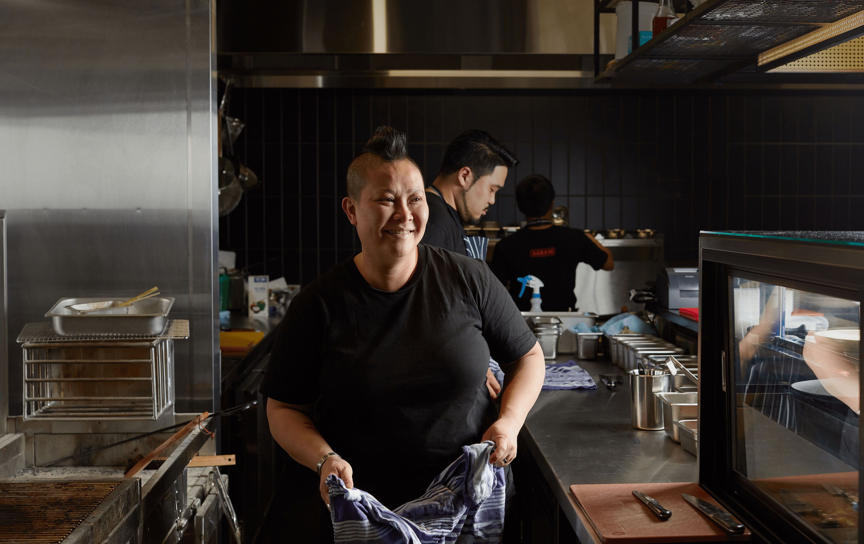 Chef Jerry Mai wearing a black t-shirt smiling in a kitchen.