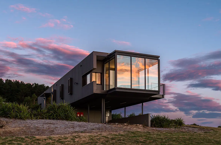 The sky is pink from the sunset, setting in front of a suspended accomodation.