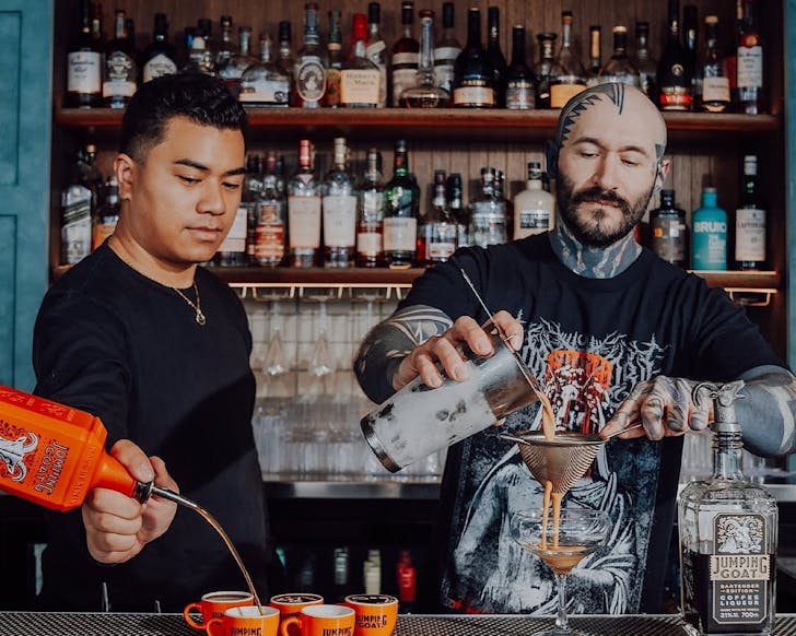 Two bartenders pour Jumping Goat coffee-infused vodka liqueur into little orange mugs.