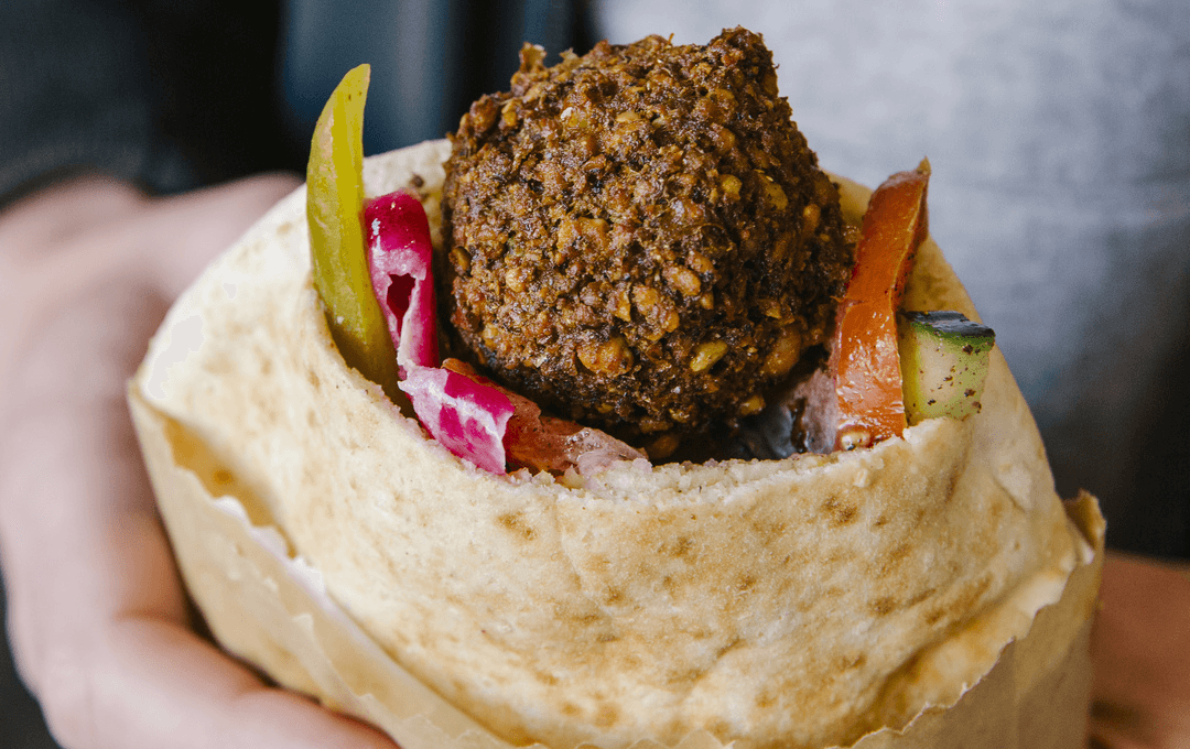 A person holding a thick pita with falafel, a best cheap eats Melbourne option. 