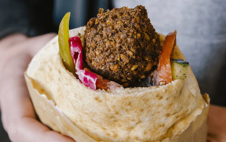 A person holding a filled falafel pita at a best middle eastern restaurant in Melbourne.