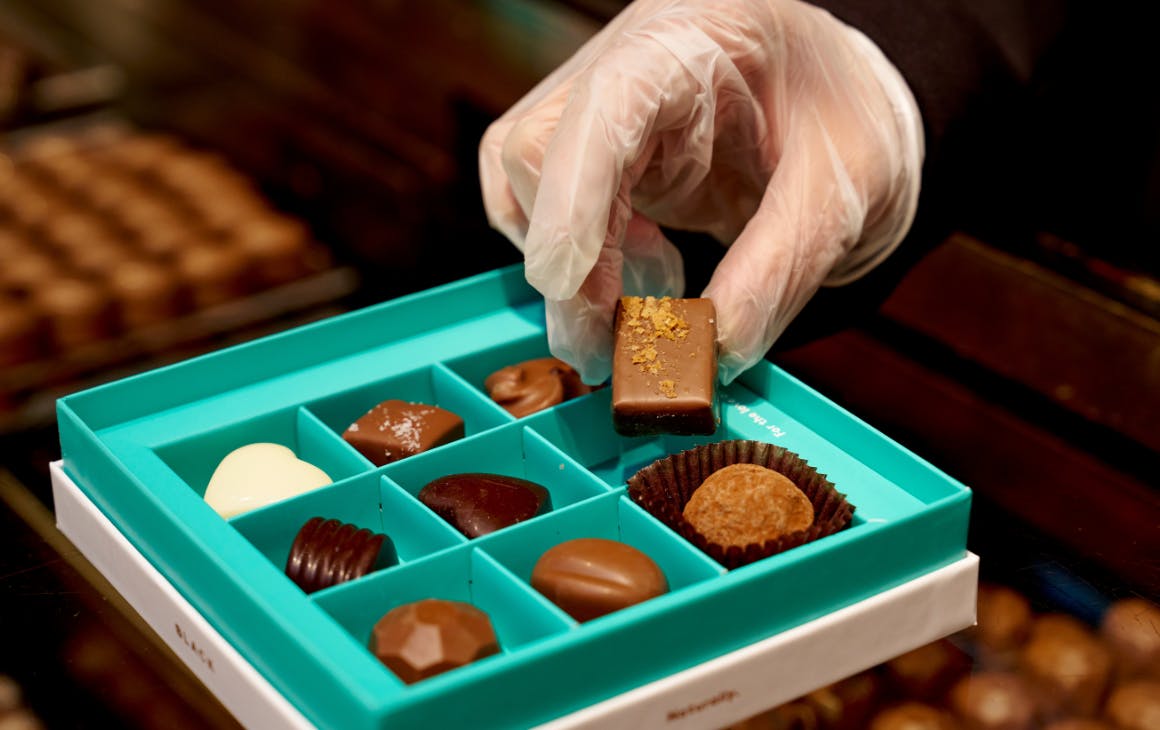 Gloved hand grabbing chocolate from a box