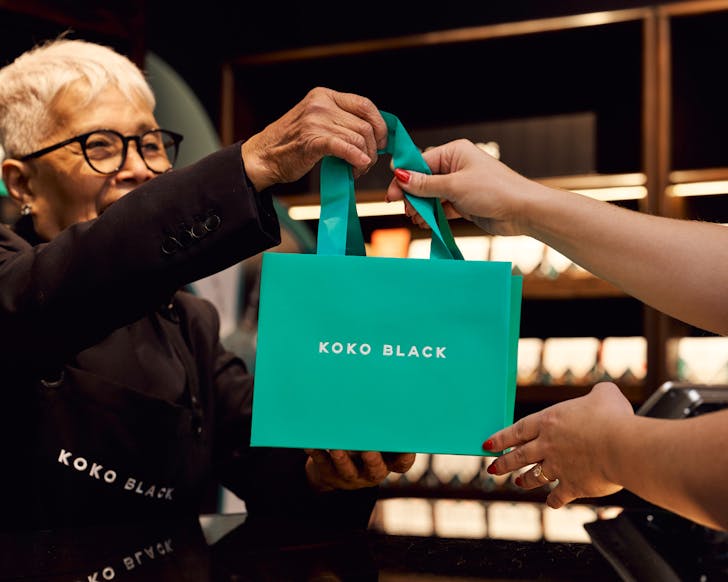 Short haired person handing medium sized blue bag to another arm of a person