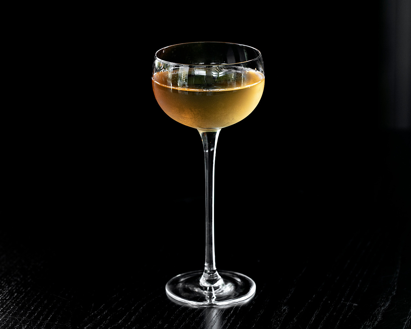 A long-stemmed cocktail glass filled with yellow liquid stands on a black background at KOL Ponsonby. 