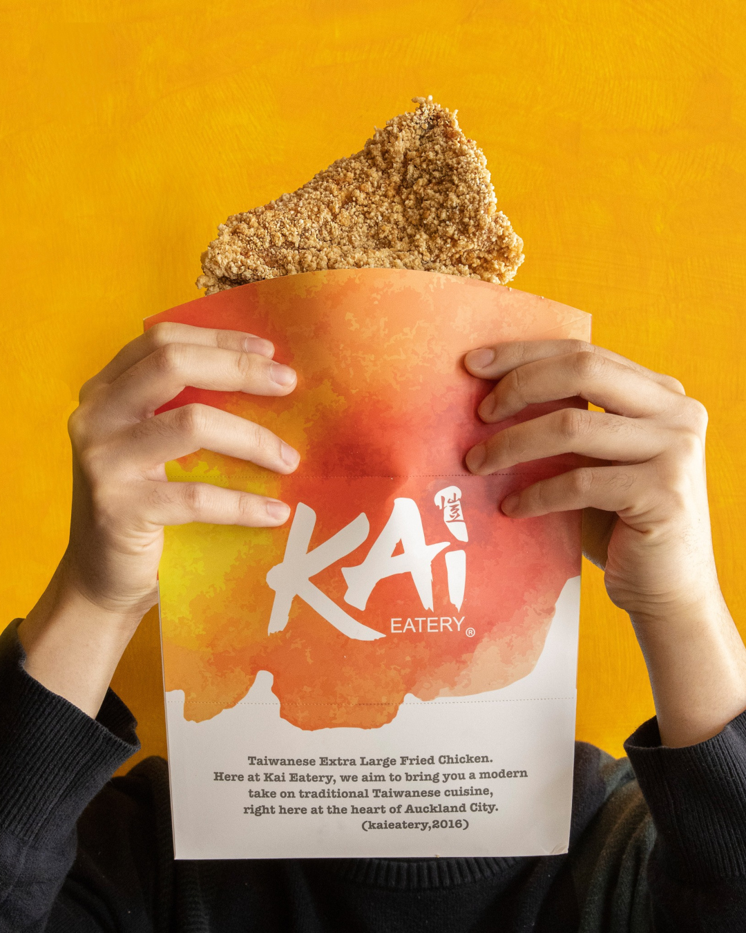 A person holds a piece of fried chicken that is literally the size of their face. 