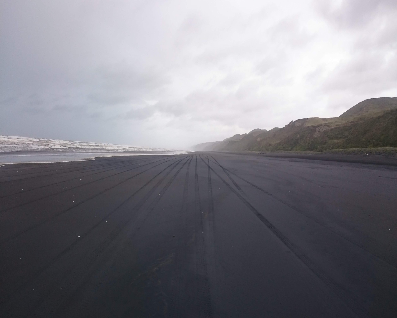 Car tracks disappearing off into the mist along the black sands of a beach. 