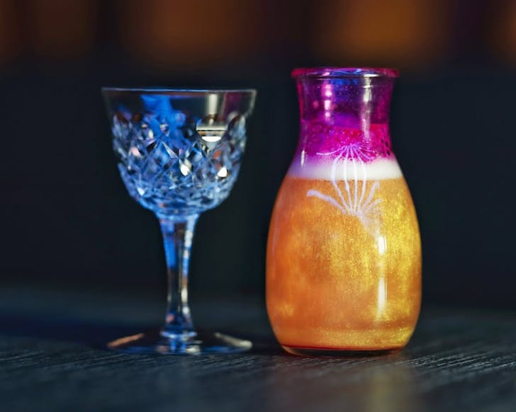A beautiful vintage wine glass and a mini carafe filled with sparkling gold and pink liquid. 