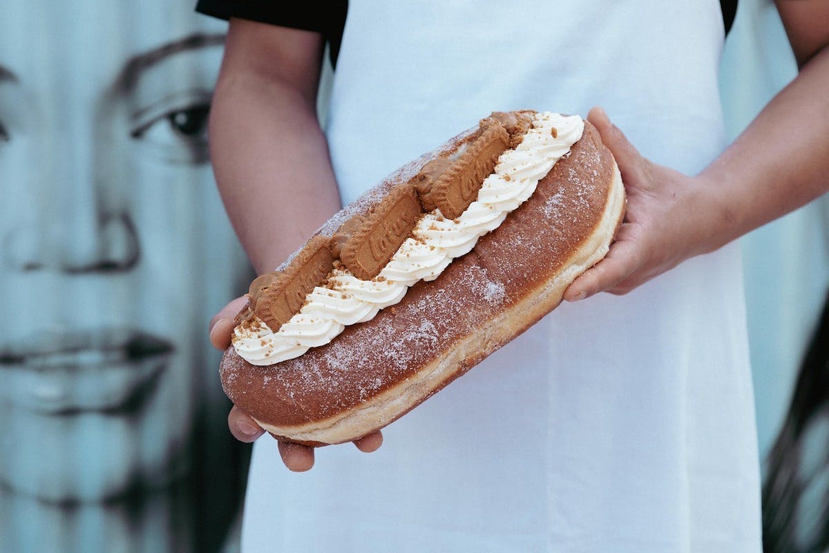 A close up of someone holding a giant doughnut topped with Lotus biscuits