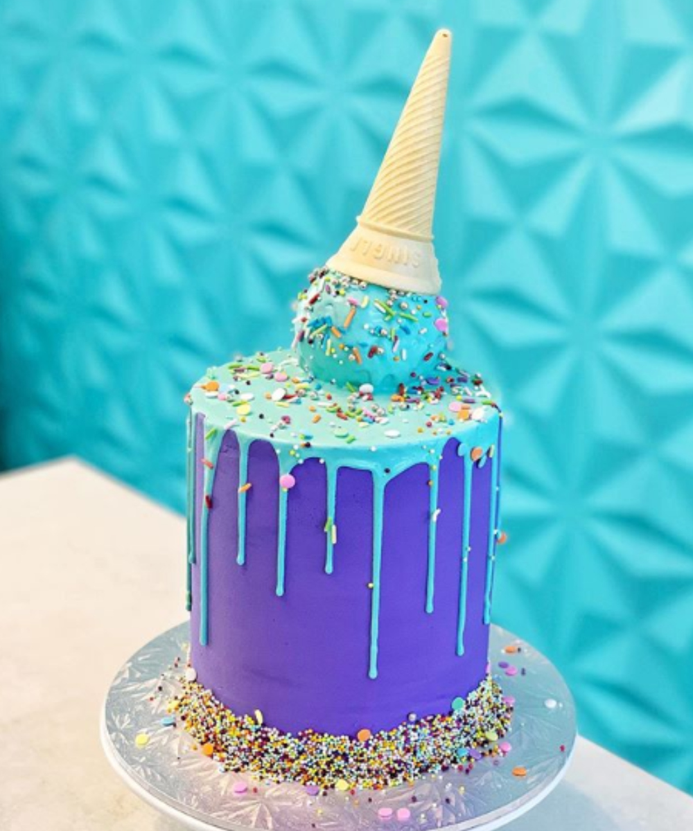 A cake decorated with an up-turned ice cream sits infront of a bright blue wall. 