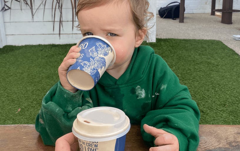 A small child in a green jumper holding a small coffee cup. 