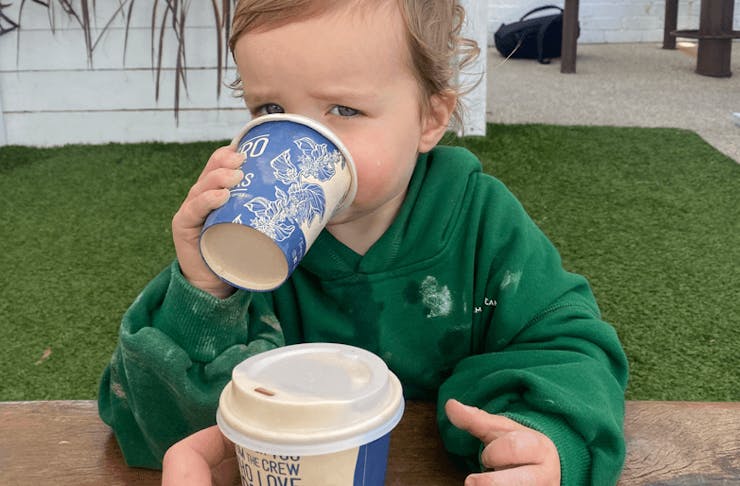 A small child in a green jumper holding a small coffee cup. 