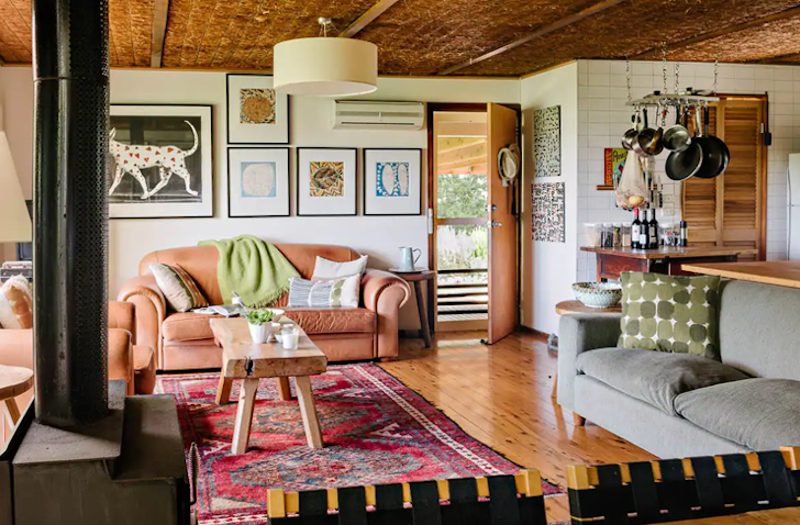 A salmon-coloured couch sits in a Airbnb with a red rug on the ground.