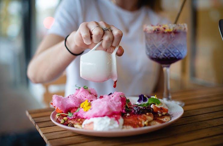 A girl pours a delicious looking sauce onto a colourful plate of breakfast goodies.