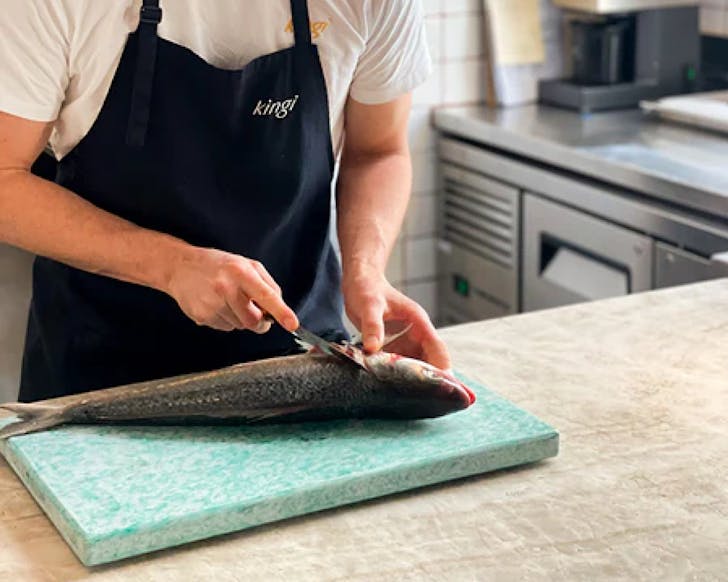 A chef starts to fillet a fish over the kingi chopping board. 