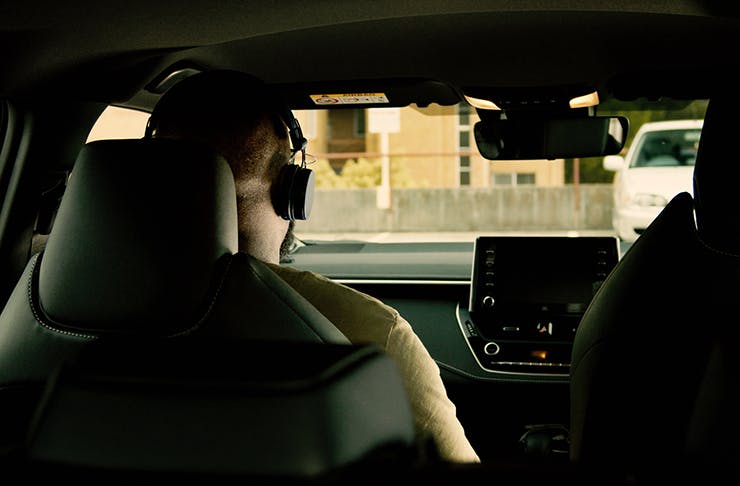 A shot from the backseat of a car with someone in the front seat wearing headphones.
