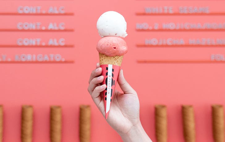 A person holding up a two-scoops of some of the best ice cream in Melbourne with a red background.