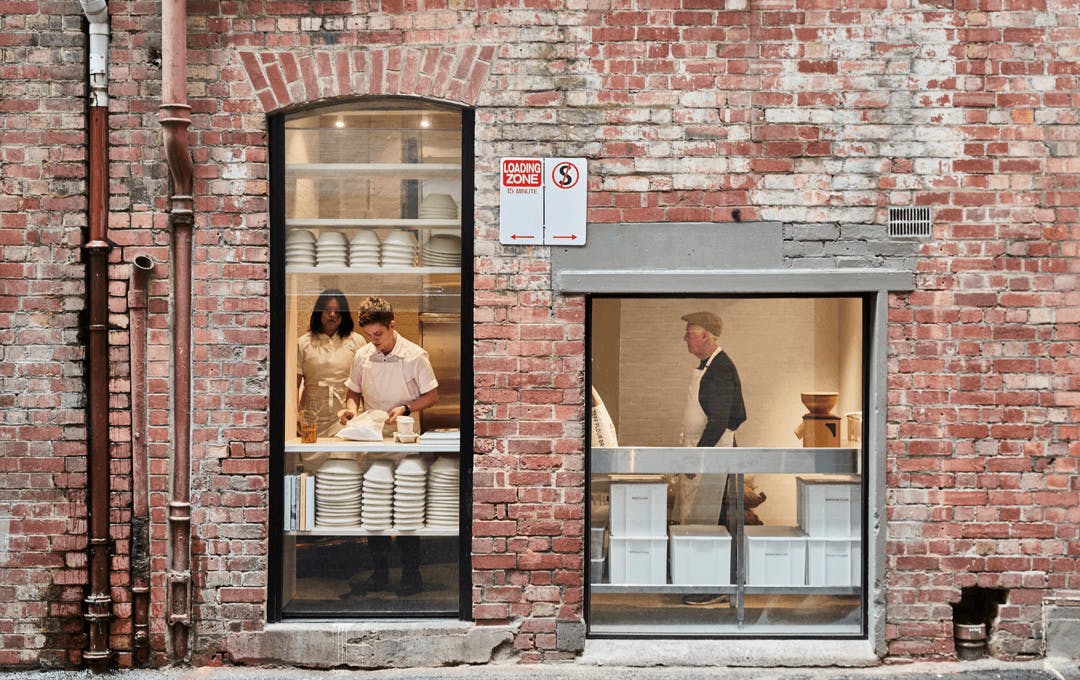 A brick wall with glass windows looking into a bakery. 