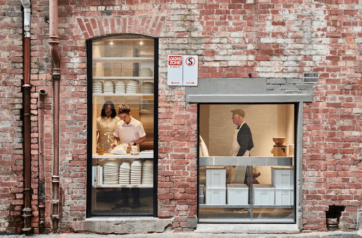 A brick wall with glass windows looking into a bakery. 