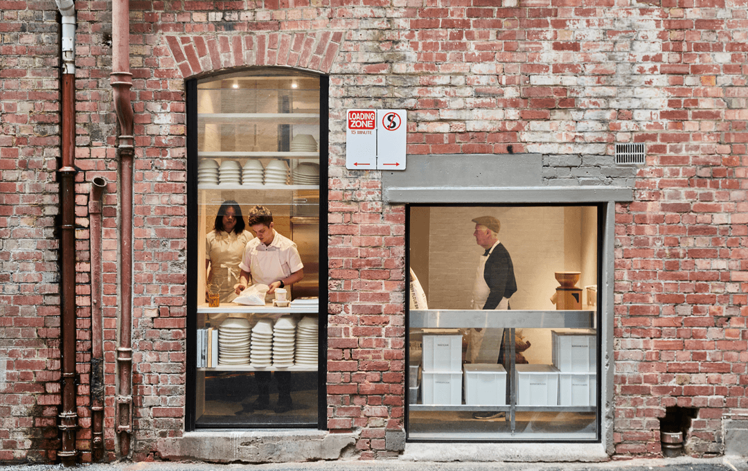 A brick wall with glass windows looking into a bakery. 