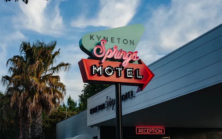 A motel with palm trees and a neon sign.