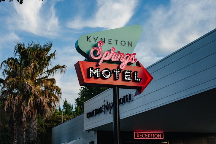 A motel with palm trees and a neon sign.