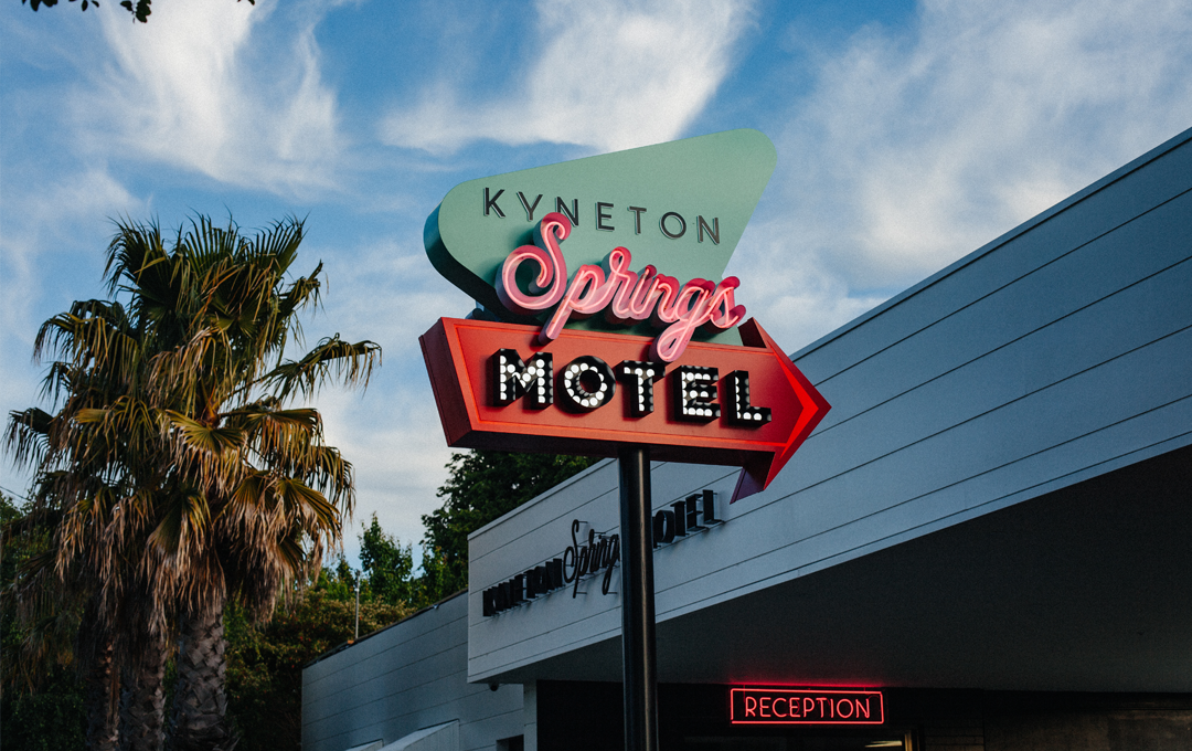 A motel with palm trees and a neon sign.
