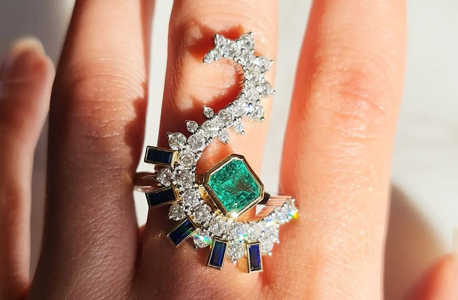 Someone wears an incredible s-shaped diamond and emerald ring. 