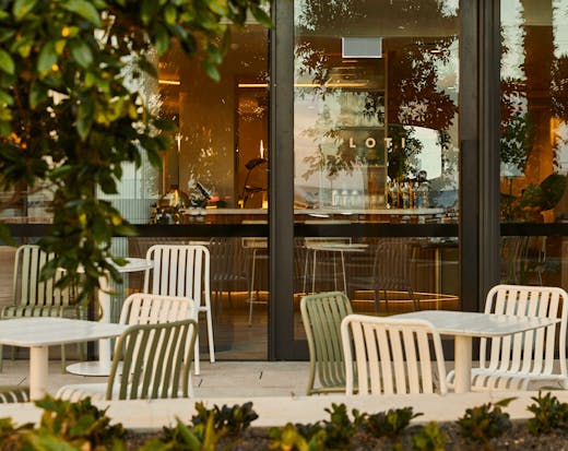 An outdoor dining area with over hanging trees and chairs and tables.