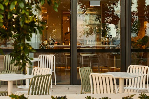 An outdoor dining area with over hanging trees and chairs and tables.