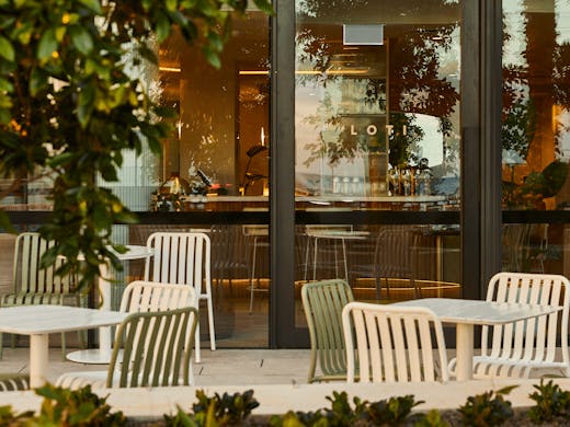 An outdoor dining area with over hanging trees and chairs and tables.
