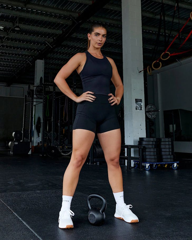 A woman stands over a kettlebell wearing an LSKD black flow performance tank. 