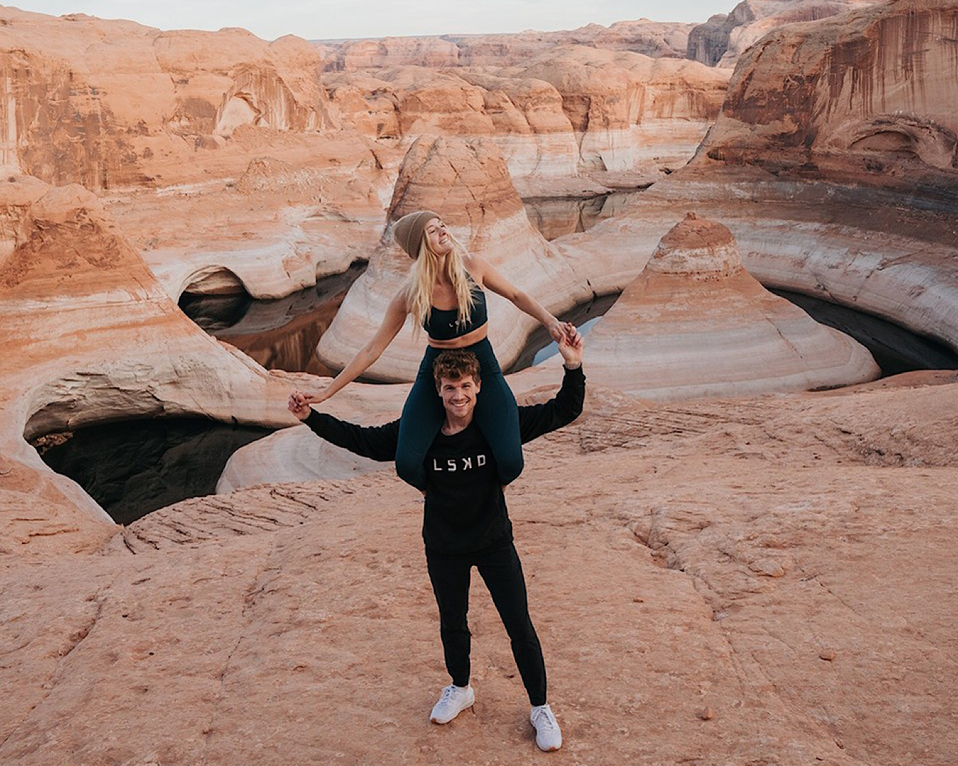 Travel Creator Karlie Place sits on a man’s shoulders in a canyon, both where LSKD activewear. 