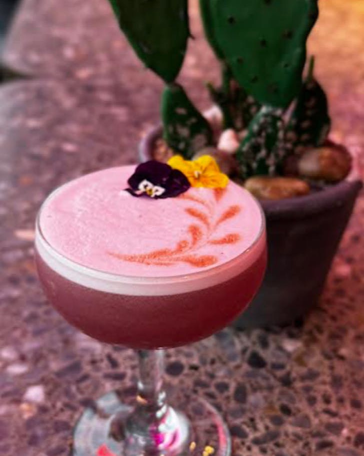 A La MaÃ±ana cocktail stands in front of a dark green classically-shaped actus. 