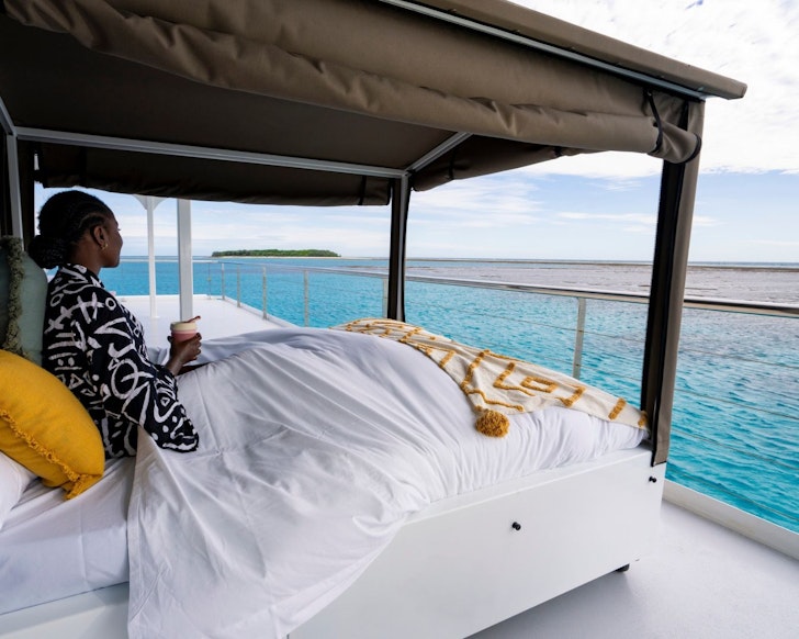 A woman lies in a bed on the deck of Lady Musgrave in one of the best glamping spots in Queensland